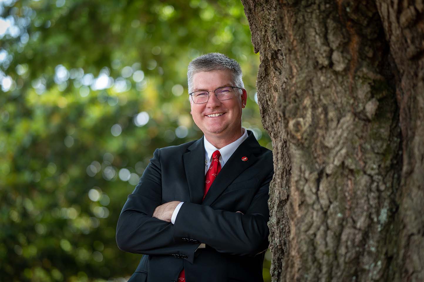 Man in a suit leaning against a tree and smiling