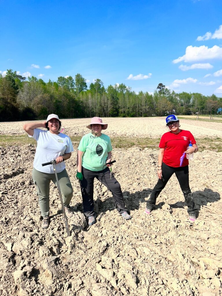 Three women standing in a dirt field