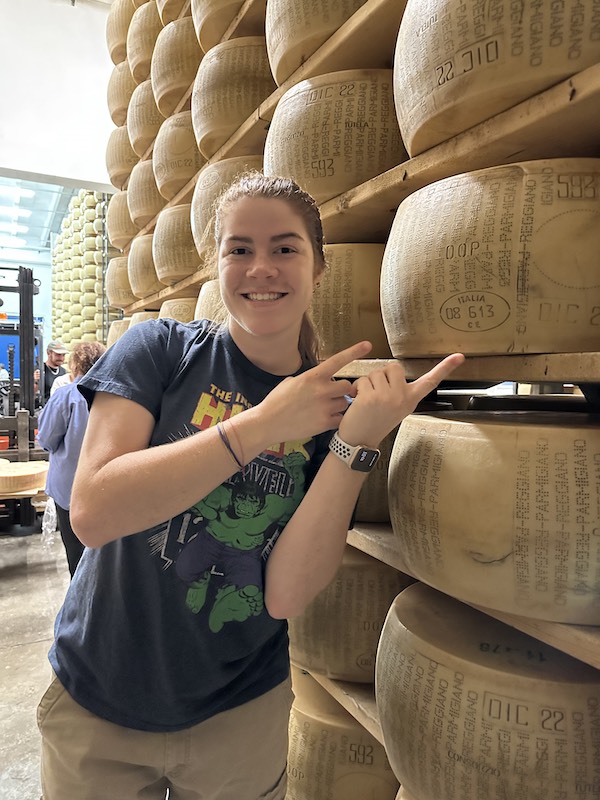 McKenzie Cummings standing next to aging parmesean cheese in Europe