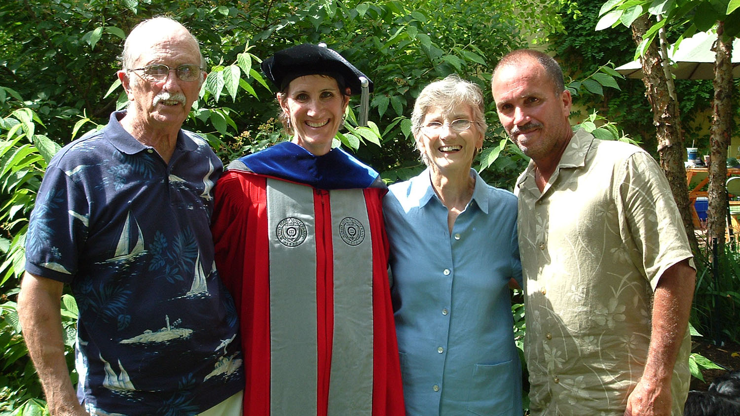 a woman wearing graduation regalia with two men and a woman