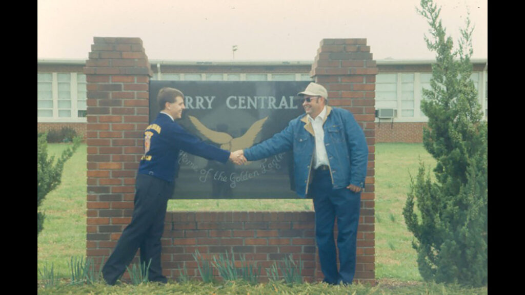 an old fashioned photo of a young man shaking hands with an older man in front of a sign