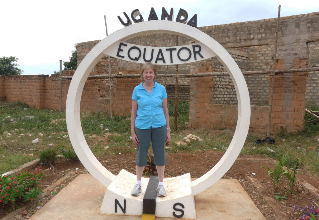 a woman stands in front of a sign that says Uganda and Eqator