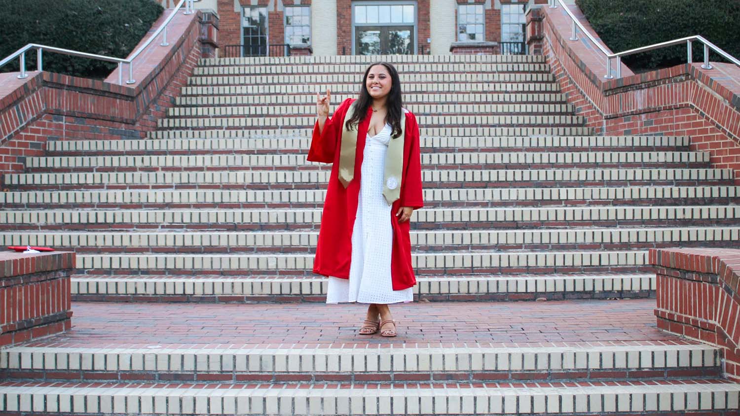 a woman wearing a red graduation gown stands on brick stairs