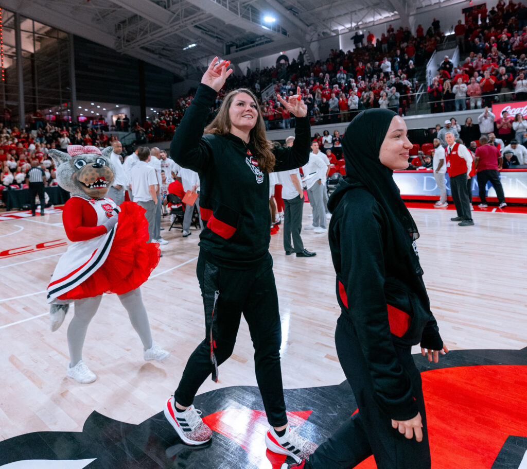 Baldwin walks on court making a Wolfpack sign with her hands
