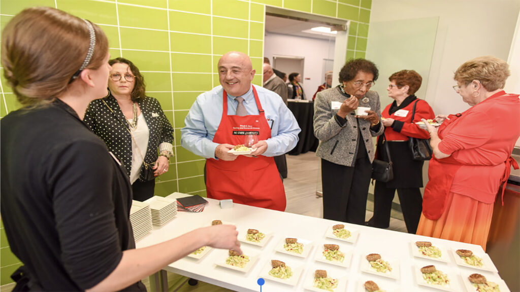 people stand around a tray of food in a commercial test kitchen