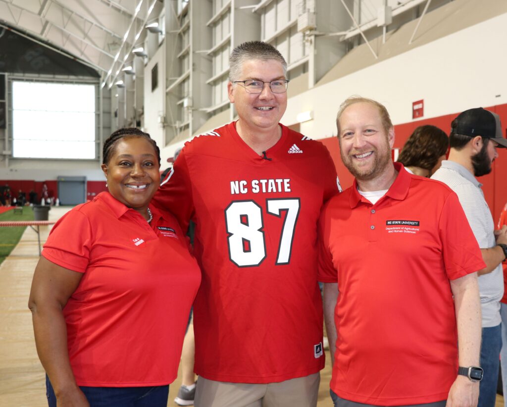 Woman and two men in red shirts smiling