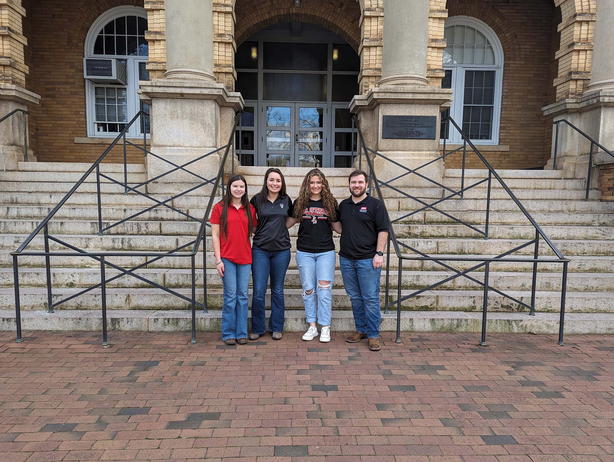 Three female and one male student standing in front of building steps