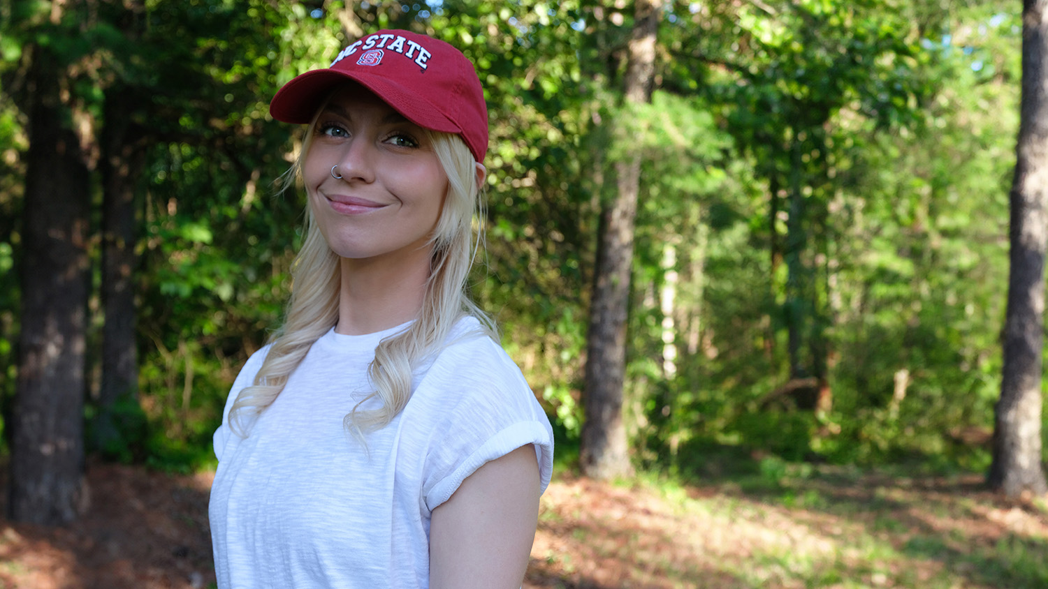 a woman wearing a red hat and white shirt stands in front of some trees