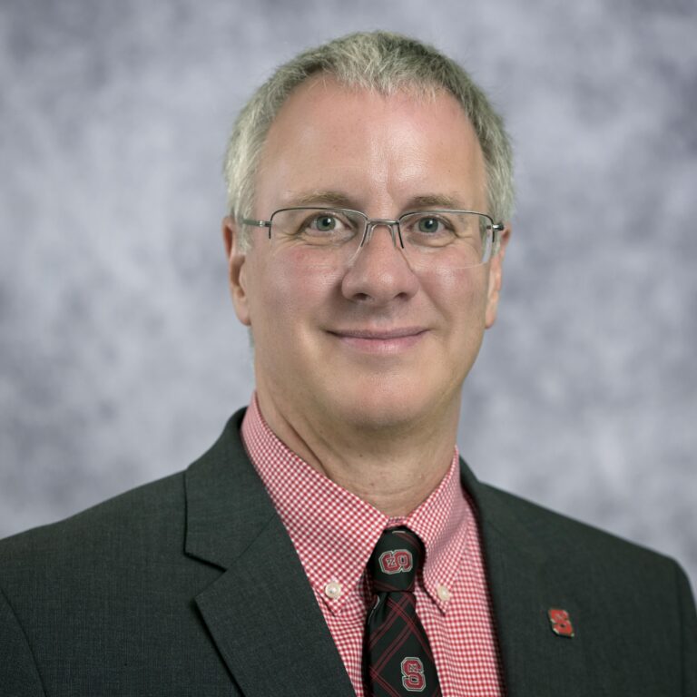 Man with glasses in suit, red shirt, and tie