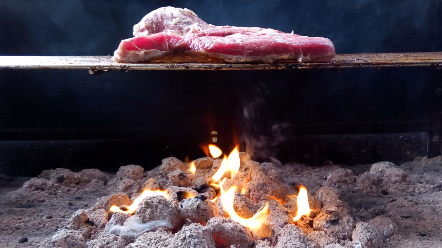 side view of a steak on a grill above hot coals
