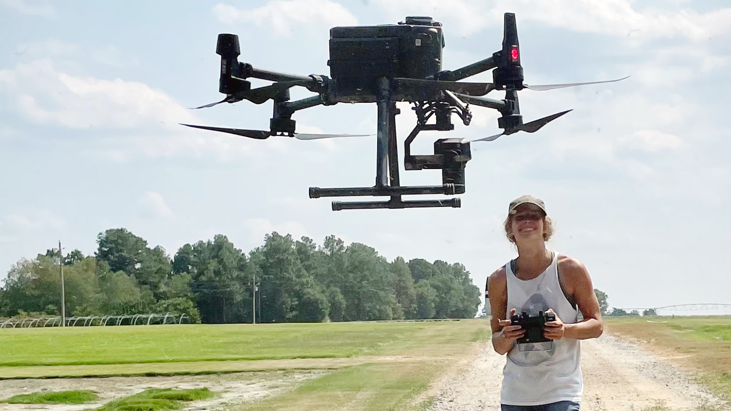 a woman flies a large drone over a turf grass field