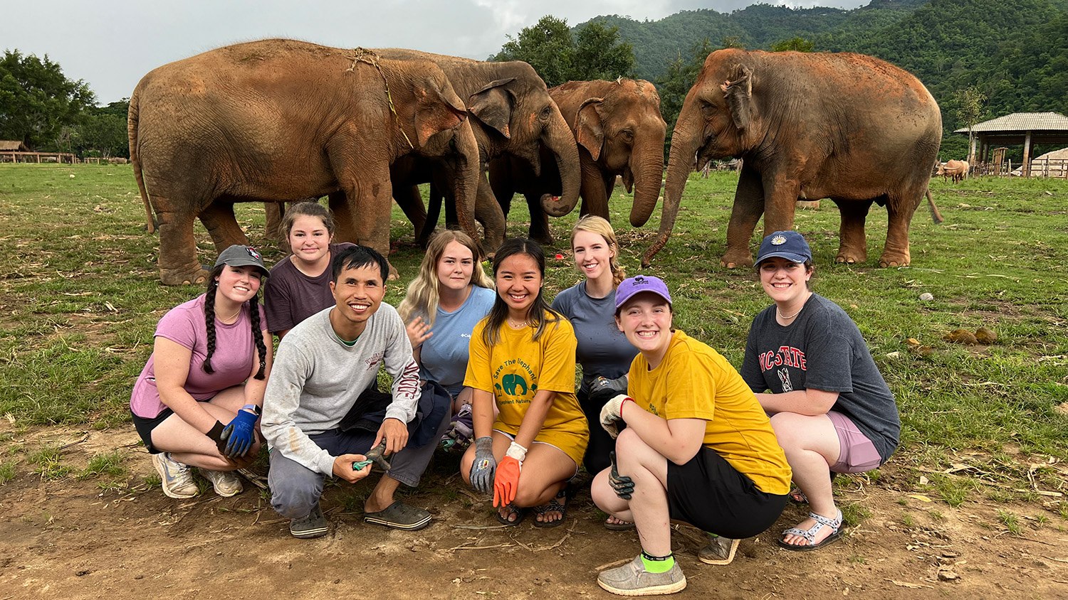 Group of students kneeling with elephants in background