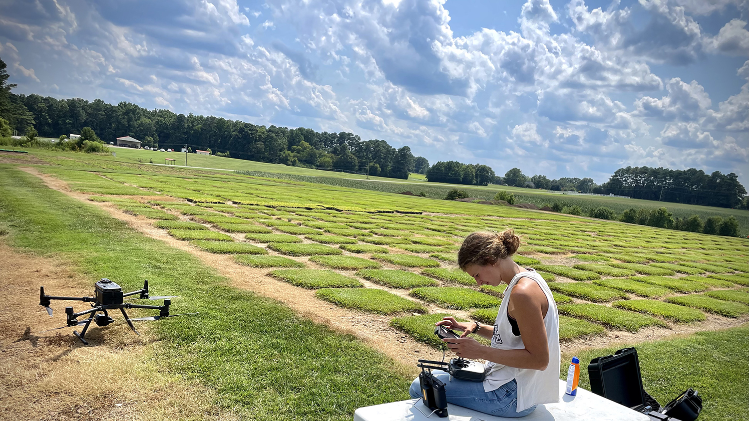 a student flies a drone in a field of turf grass plots