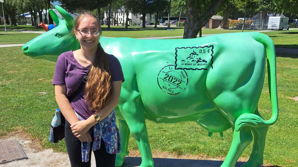 Young woman in purple top standing in front of a green cow