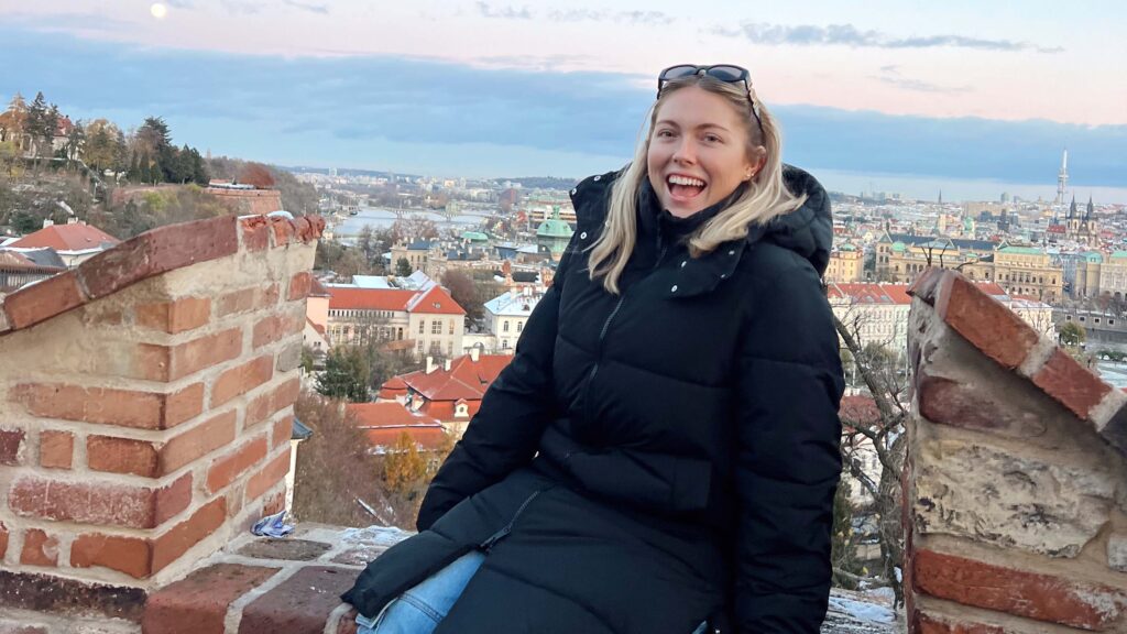 Blond young woman in black coat smiling on rooftop