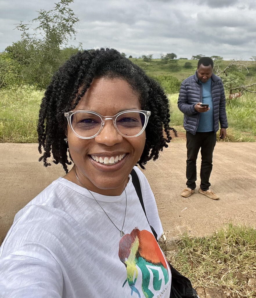 a woman stands outside with trees and tall grass behind her