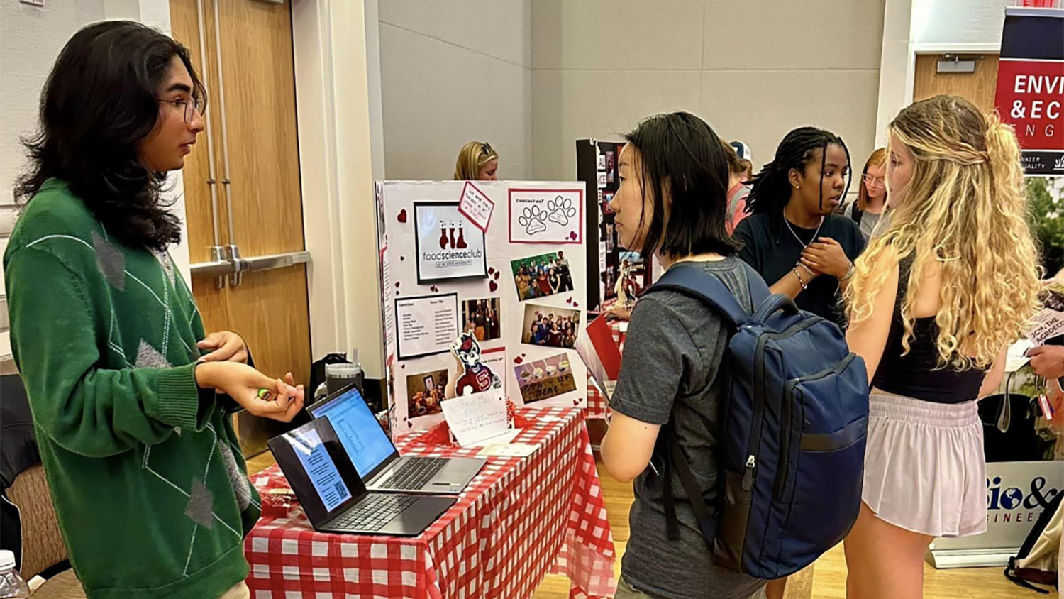 students stand at a table with a poster behind them