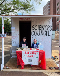 Two students sitting at small table in front of a shack