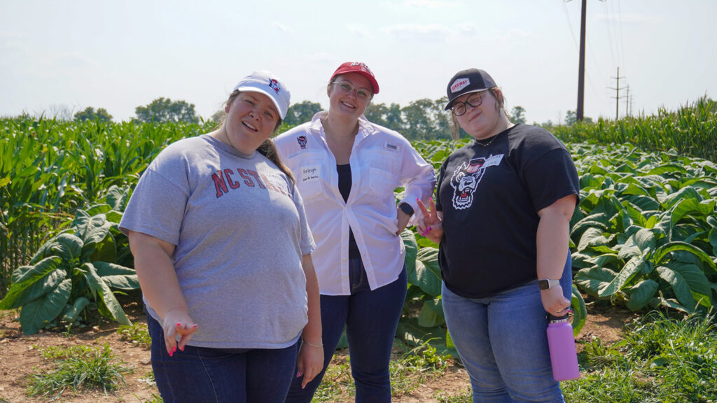 three women stand on a crop field