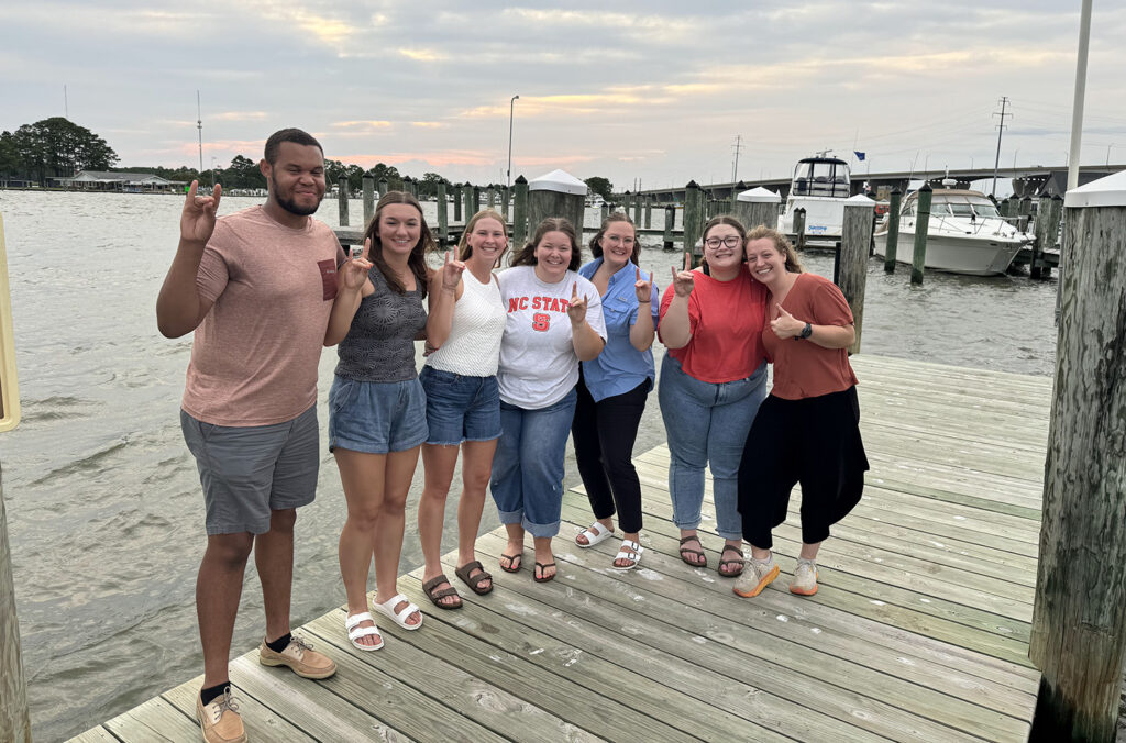 a group of people stand on a dock next to a river