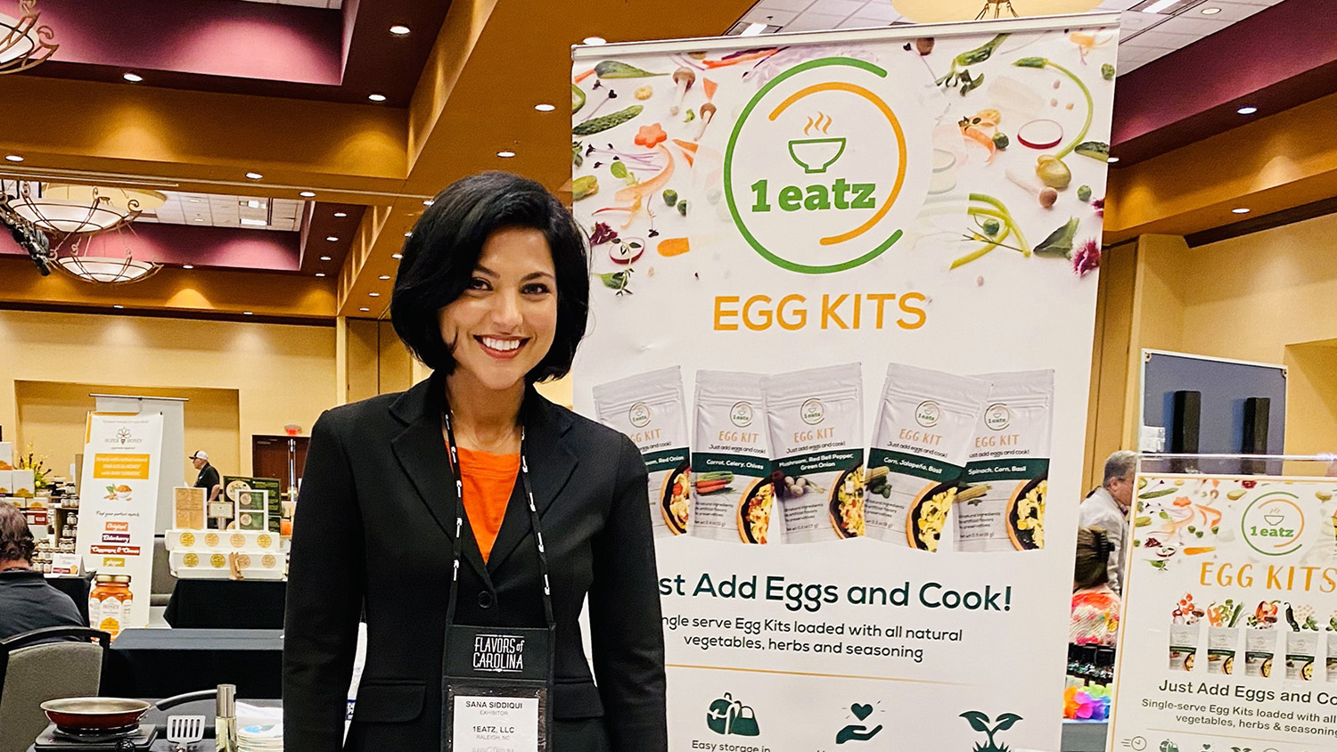 sana siddiqui stands next to a 1eatz display