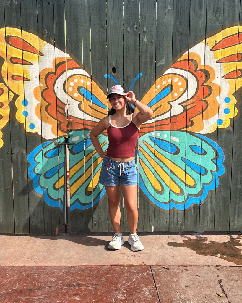 Young woman in red top and shorts in front of butterfly painting