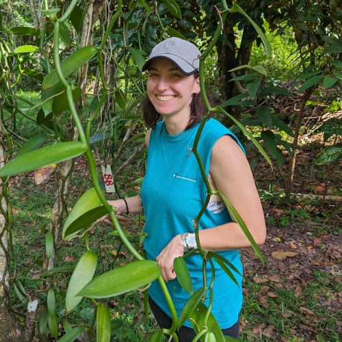 Young woman in blue top and cap standing next to a large plant