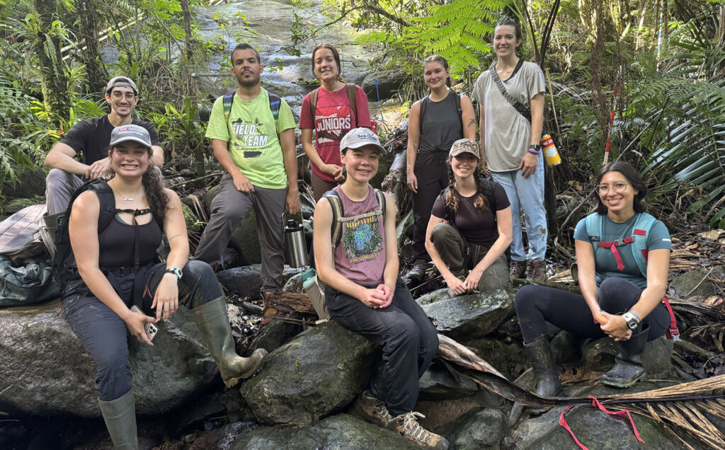 a group of people sit by a rocky stream bed