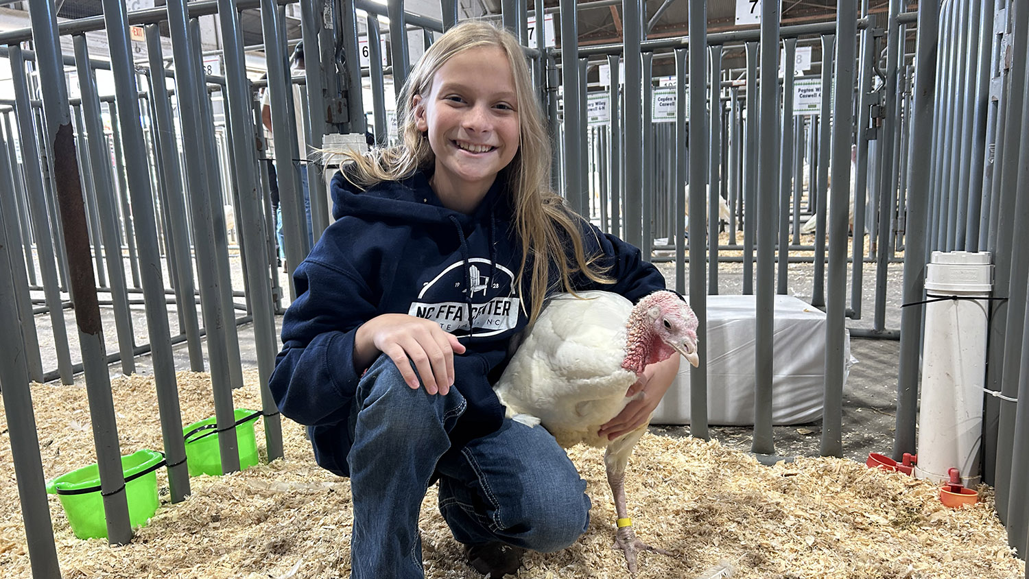 a girl sits in a pen with a turkey