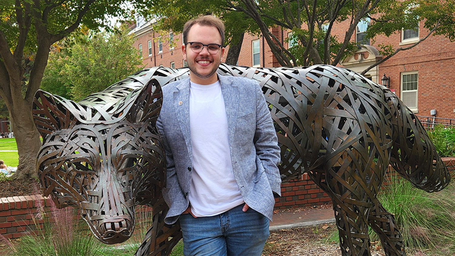 Young man with glasses leaning on a wolf sculpture