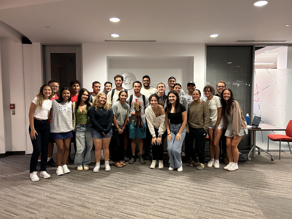 Group of students posing and smiling in a carpeted classroom