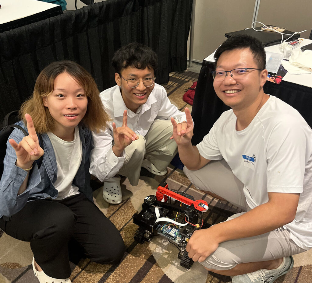 three people posing with a small robot