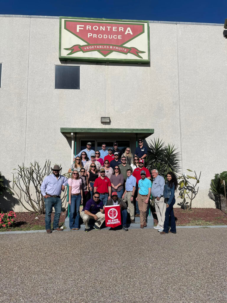 a group of people standing outside a building with a sign that says Frontera Produce