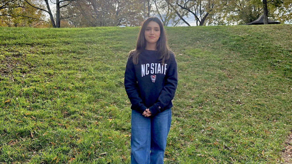 a young woman stands outside on a grassy field