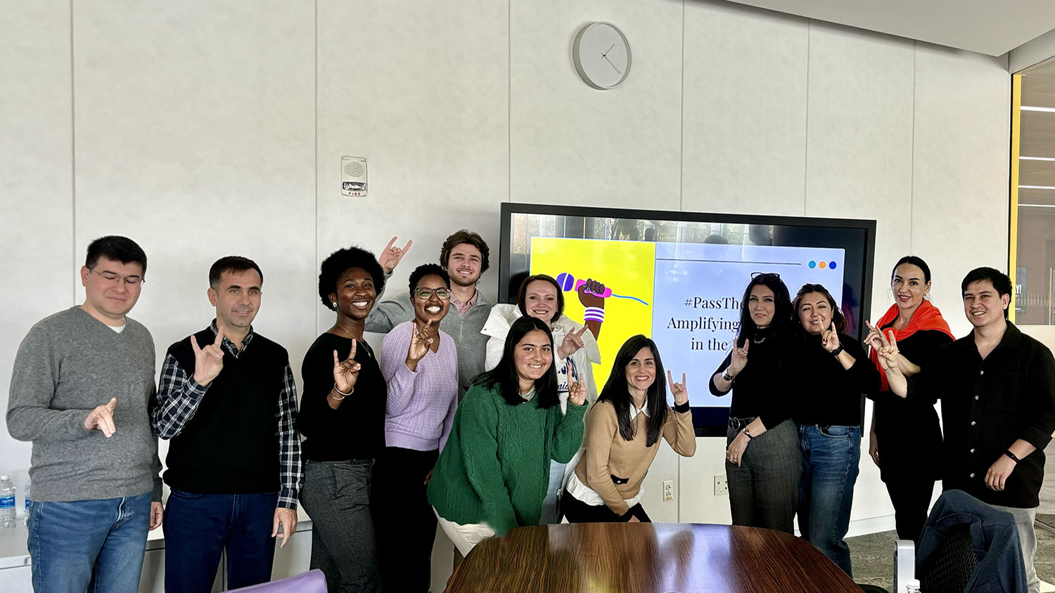 a group of people standing in front of a digital screen making the wolf sign with their hands