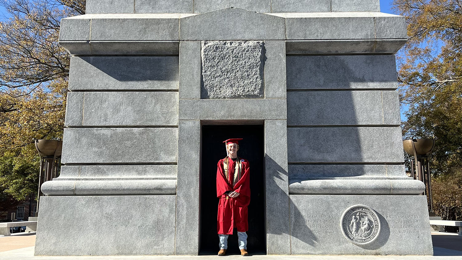 a young man wears a red cap and gown for graduation