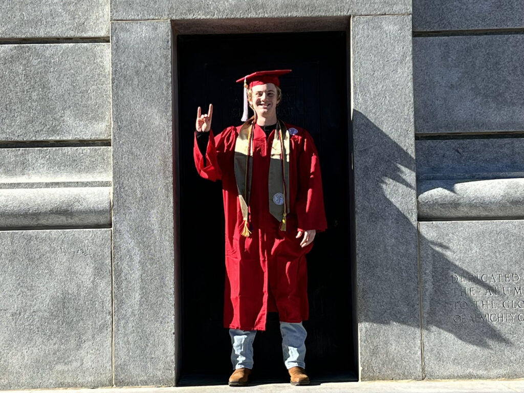 a young man wears a red cap and gown for graduation