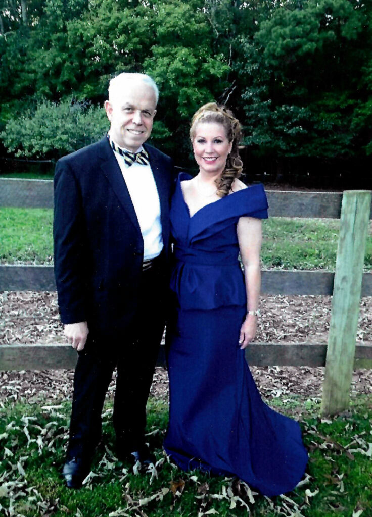 a man and woman dressed in formal attire stand next to fenced pasture