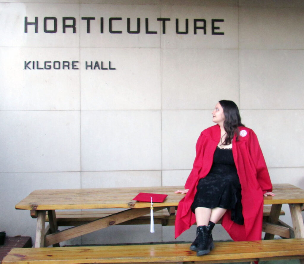 a woman wears a red gown and a black dress while looking at a sign that says "horticulture"