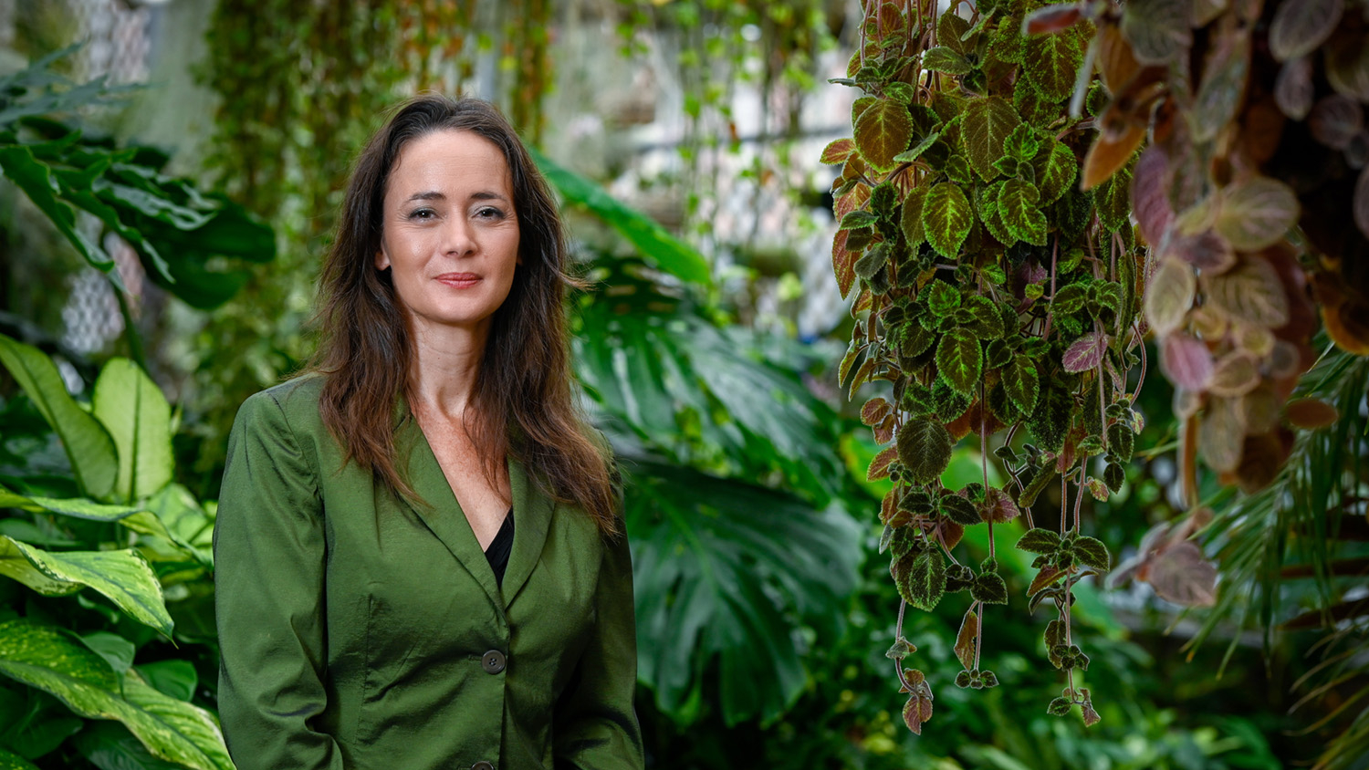 Vanessa Woods stands in a greenhouse full of green, tropical plants.