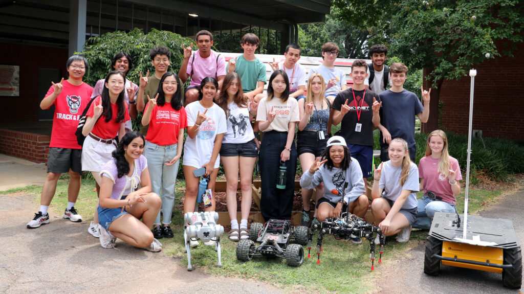 a group of students stand outside with robots while making wolf hand signs