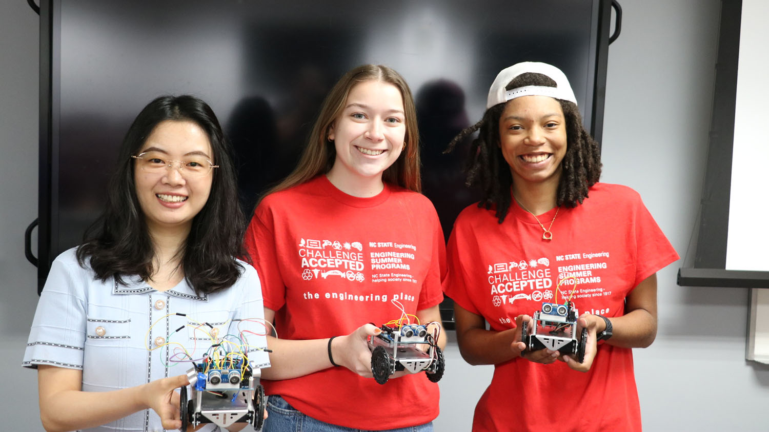 three women hold small wheeled robots