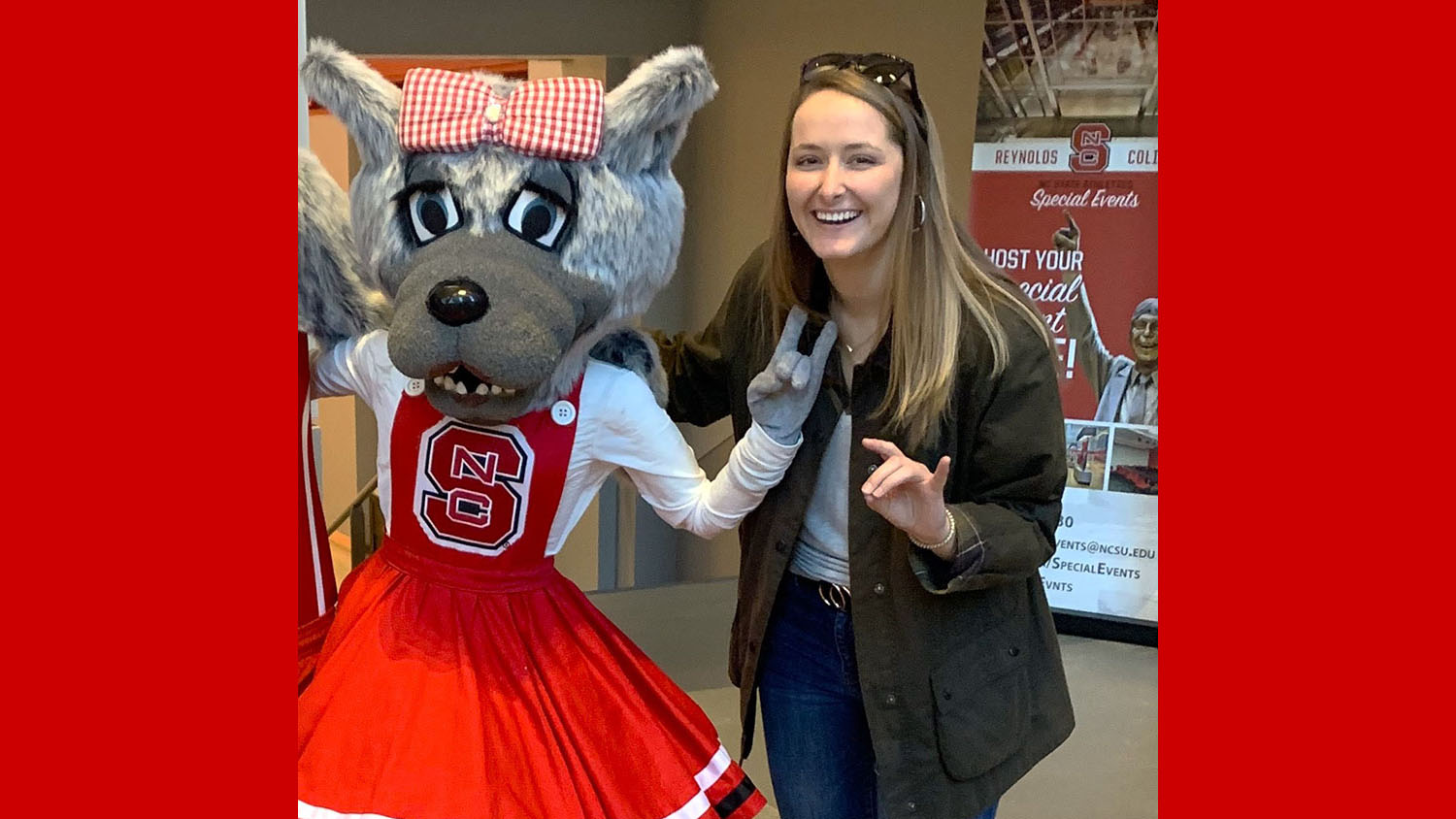 a woman stands with a girl wolf mascot making wolf signs with hands