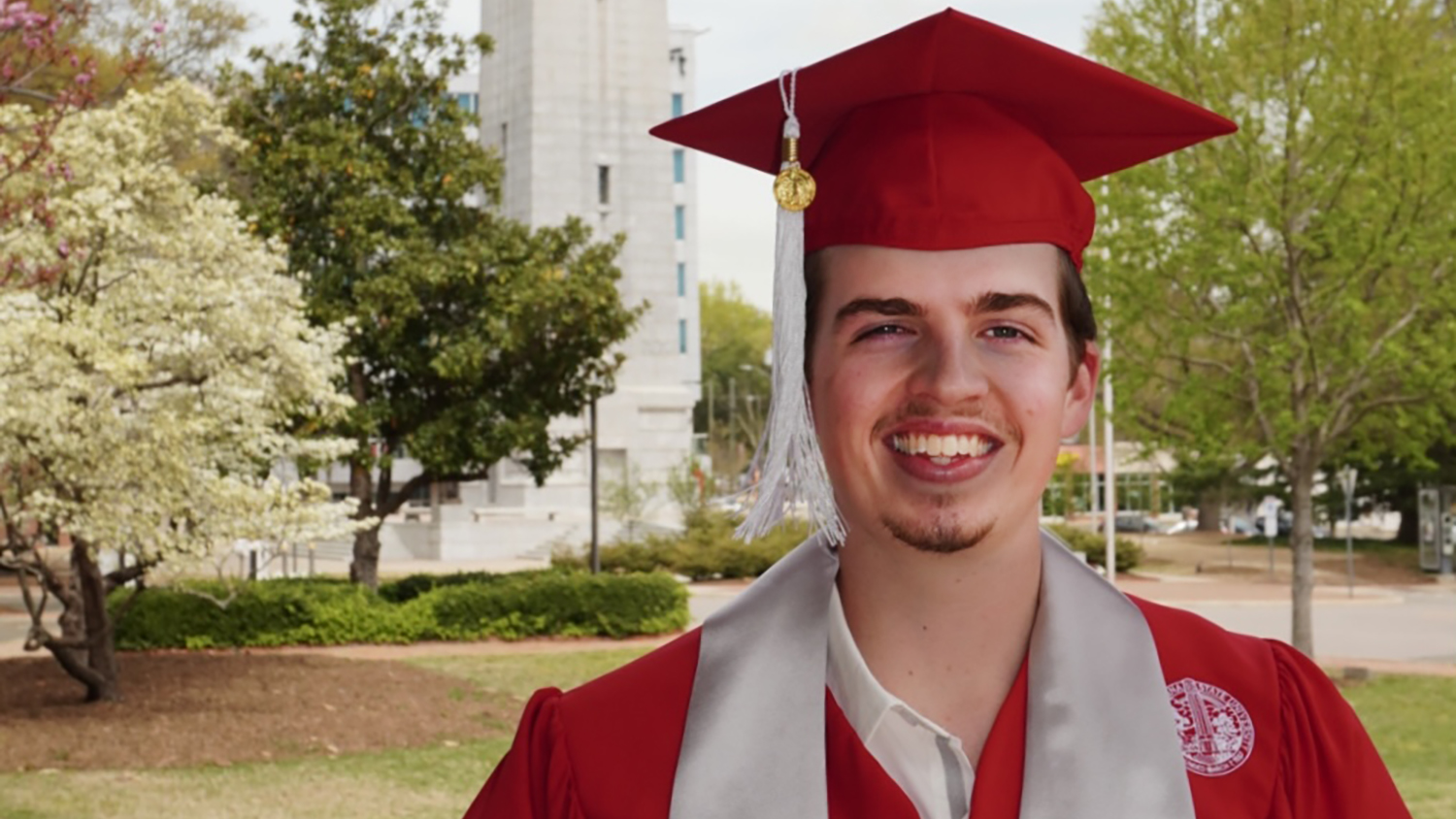 a young man in a red cap and gown for graduation standing outside