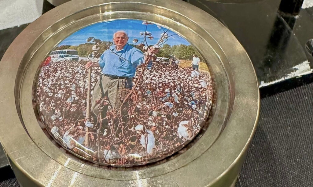 a pin button with a picture of a silver hair man standing in a cotton field