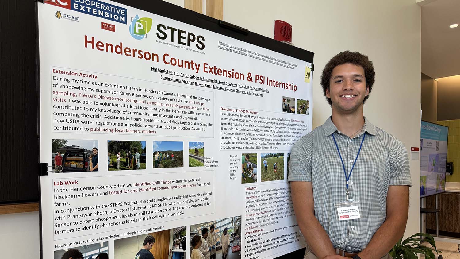 a young man stands next to a large poster that says Henderson County Extension & PSI Internship