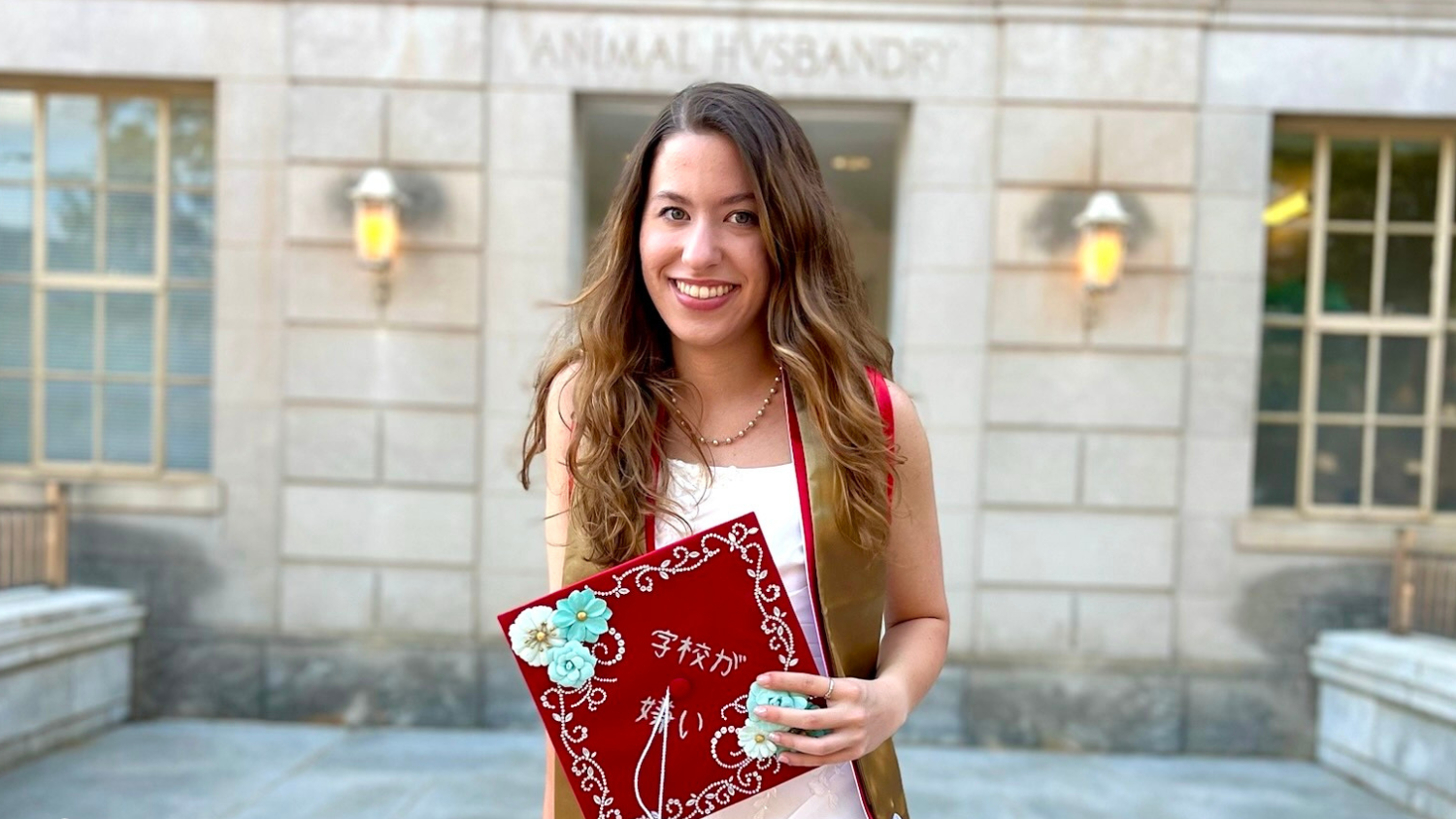 a woman holds a red graduation cap while standing in front of a grey building