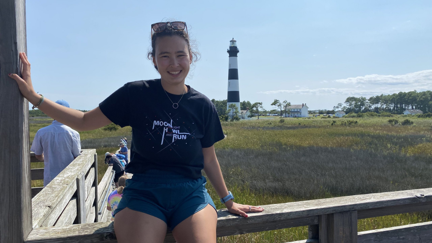 a girl sits on a fence with a lighthouse in the background