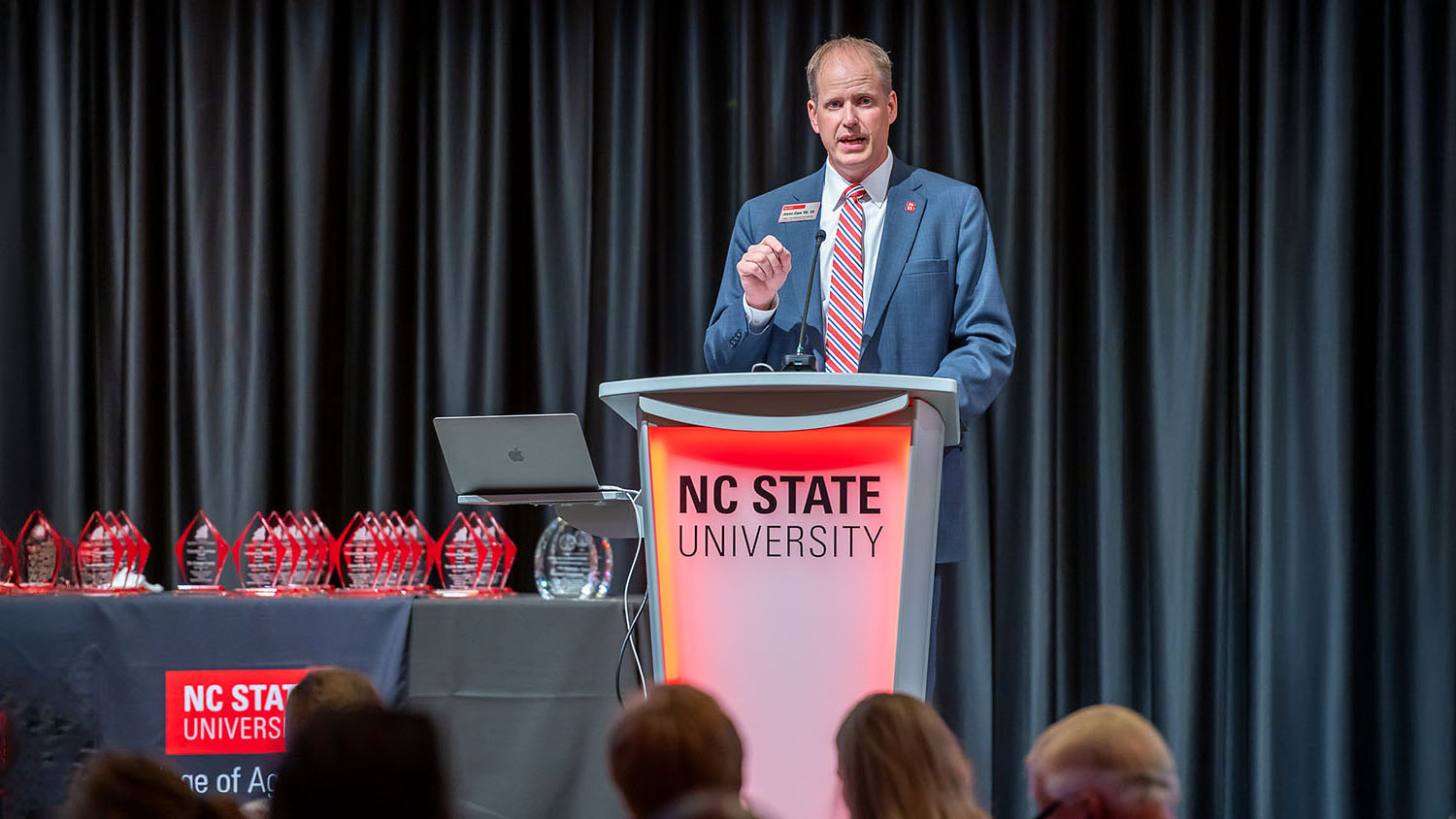 a man wearing a coat and tie stands at a podium that says NC State University