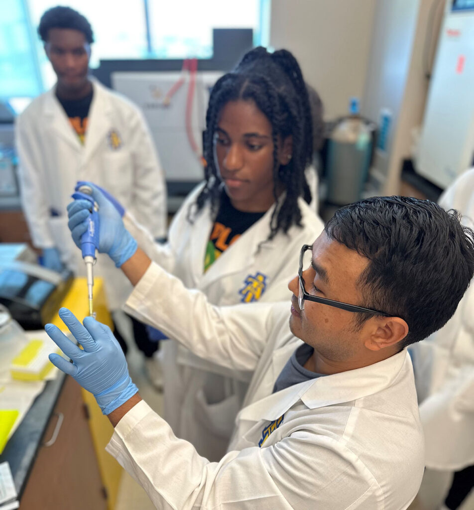 people in a lab looking on as a man uses a pipette